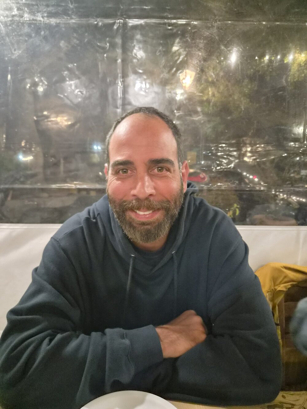 George smiling at a table, arms crossed, in a dark hoodie